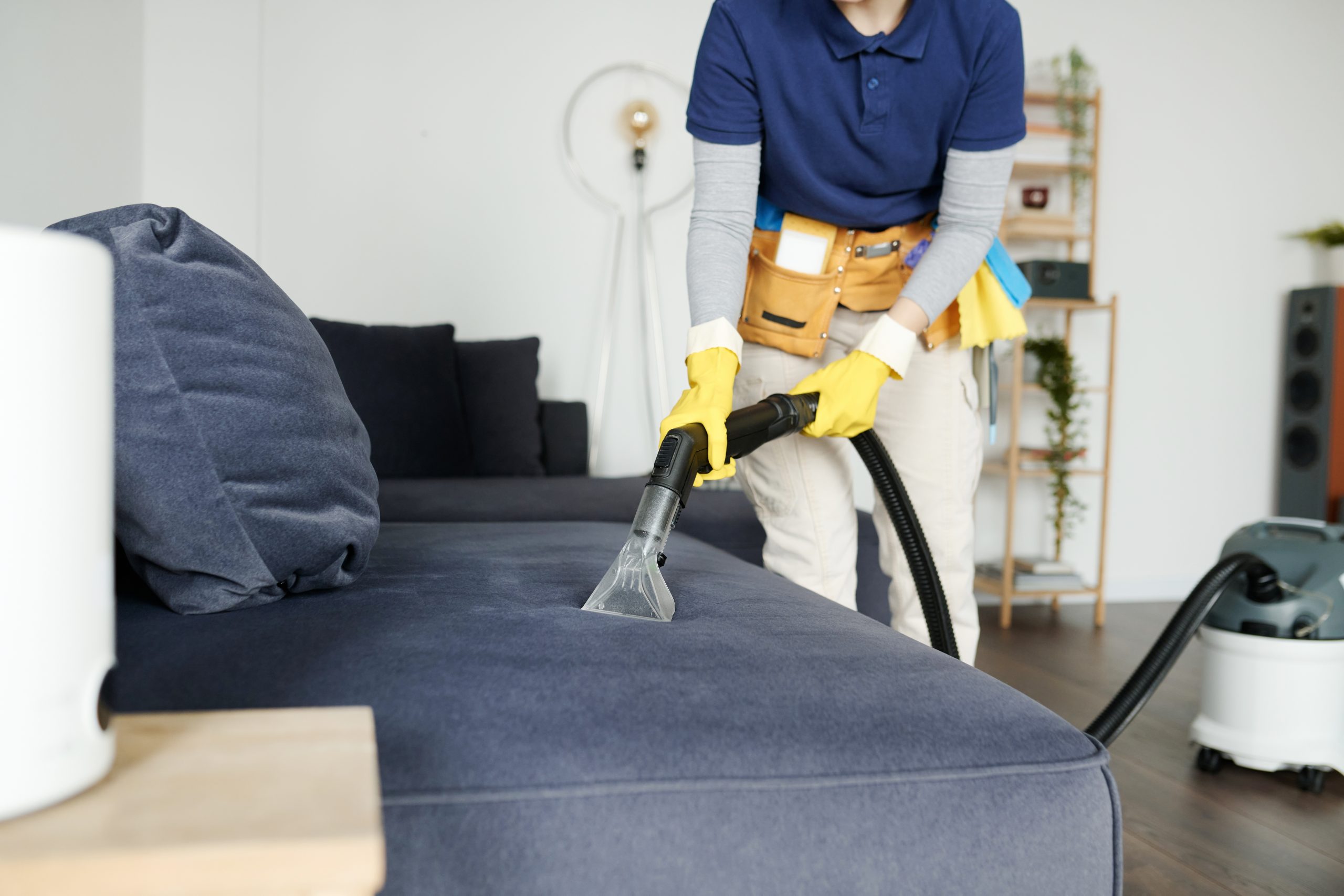 Cleaning service worker vacuuming sofa from dust with vacuum cleaner during housework maids my way belleville event and one time cleaning options